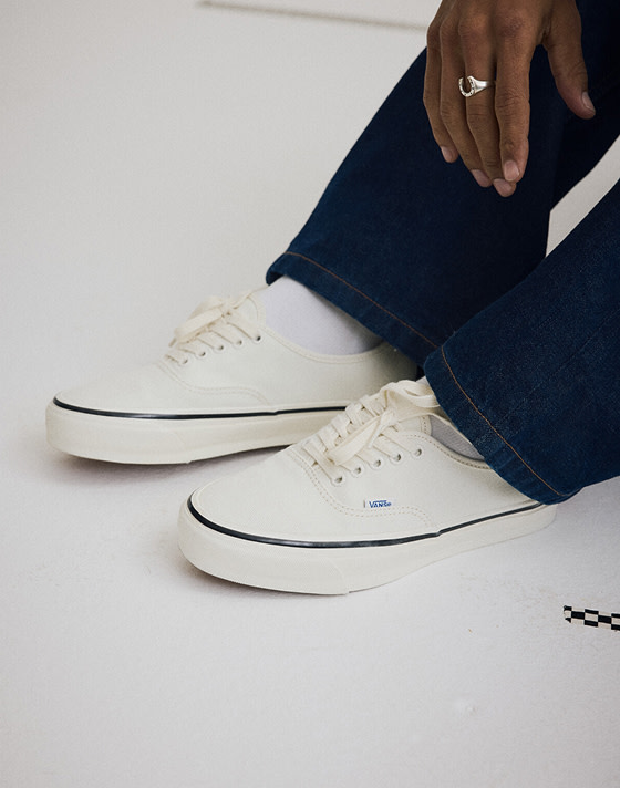 Close up of someone wearing the Premium Authentic Shoe in Marshmallow White while sitting on the ground of a grey photography studio.
