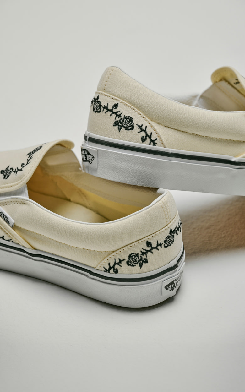 Close up on the heels of the Classic White Classic Slip-On Shoe with black embroidered roses and thorns.