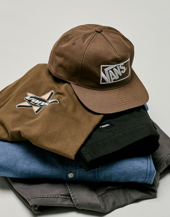 Close up of the Vintage Cocoa Brown Vans Formula Snapback Hat sitting on top of a pile of clothes in a grey photography studio.