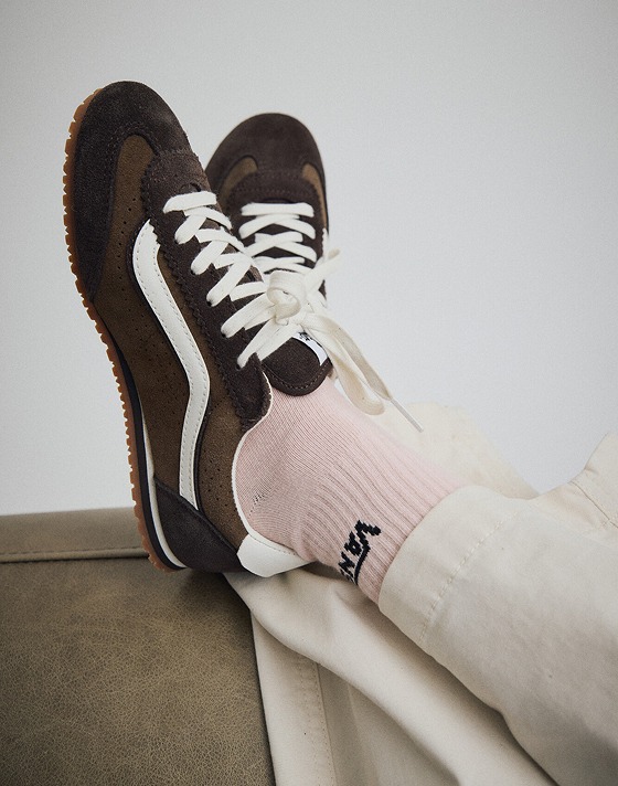 Close up of someone wearing the Demitasse Brown Super Lowpro shoes while kicking their feet up on the end of a couch.