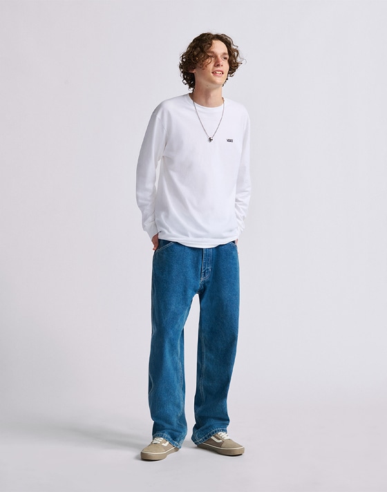 Wide shot of a man wearing the White/Black Left Chest Logo Long Sleeve T-Shirt and Vintage Indigo Blue Skate Check-5 Loose Denim Pants in a studio.