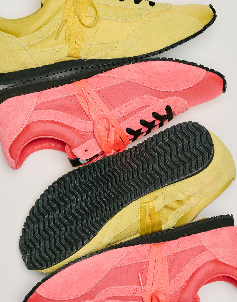 Close up shot of alternating pairs of the Premium Super Lowpro Trainer in Diva Pink and Space Yellow on the floor of a grey photography studio.