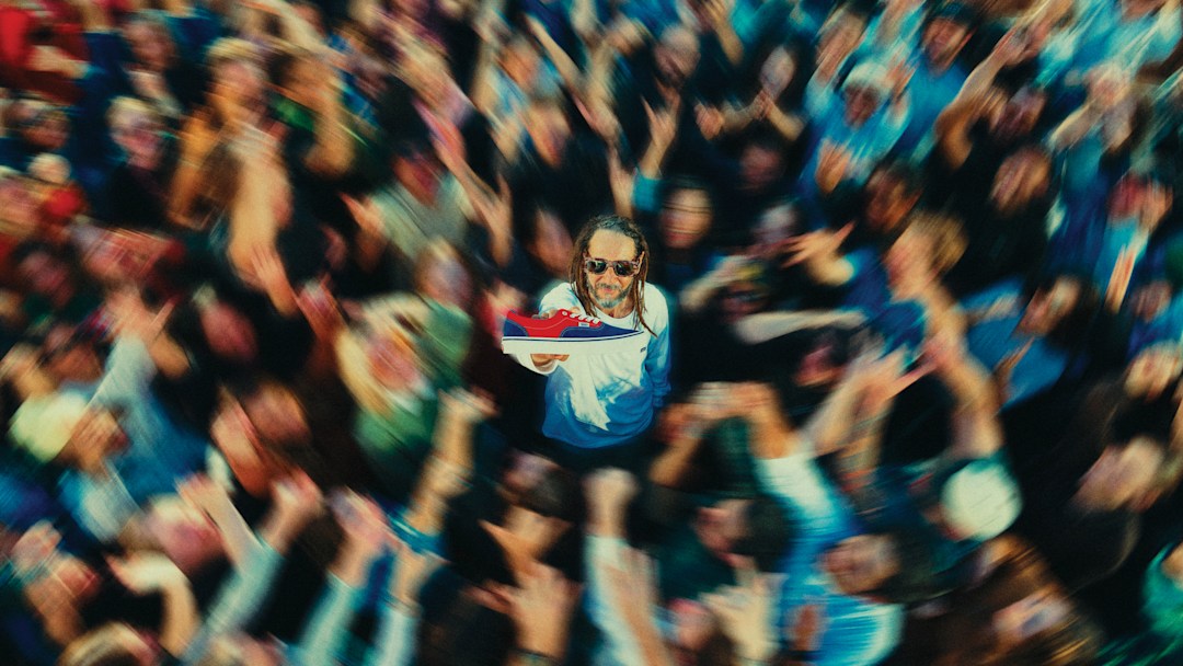 Tony Alva holding a Vans Skate Era shoe amidst an excited crowd of people.