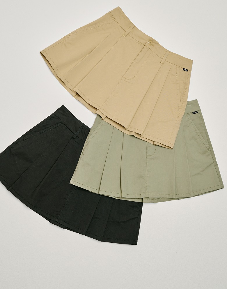 Three Authentic Chino Skirts lie on the floor of a photography studio in the incense brown, soft sage green and black colorways.