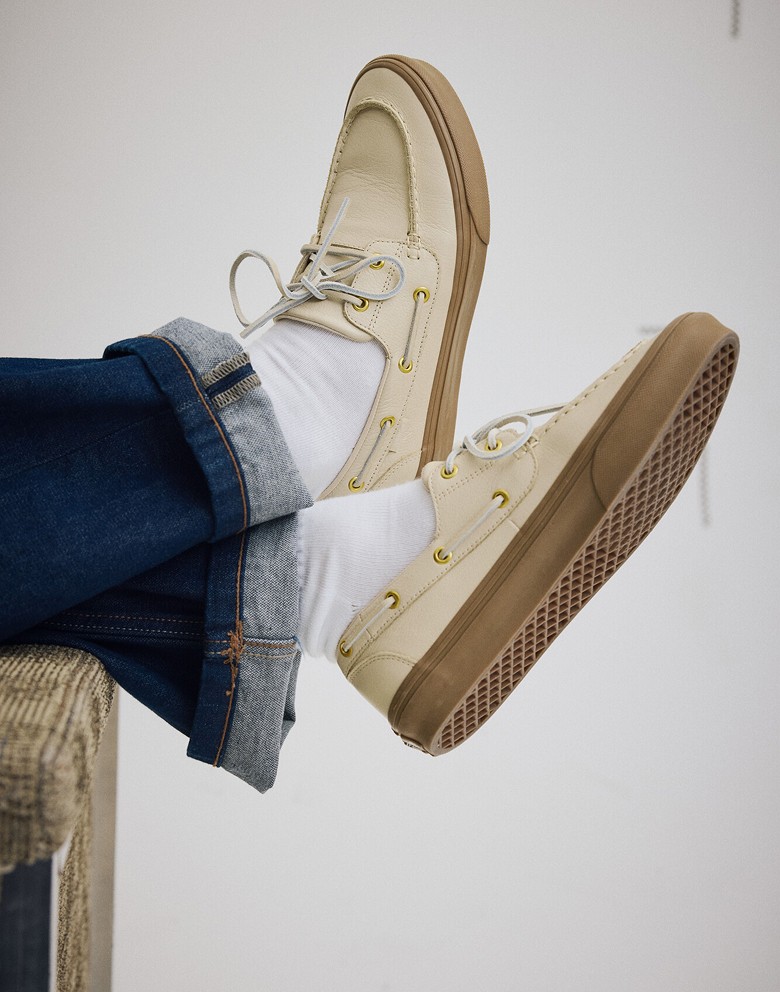 Close-up of someone wearing the tan 2-Eyelet Boat shoe over the arm of a sofa with white socks and blue jeans.
