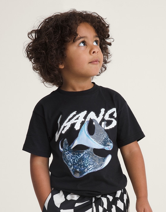 A young boy wearing black and white Little Kids Primary II Printed Elastic Boardshort in a photography studio.