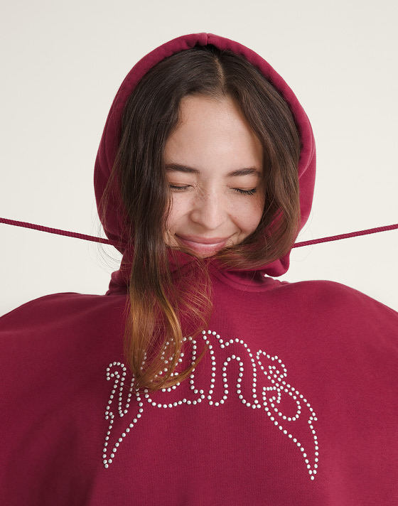 A young woman pulling on the cords of her bordeaux red Pearls Logo Retro Pullover Hoodie.