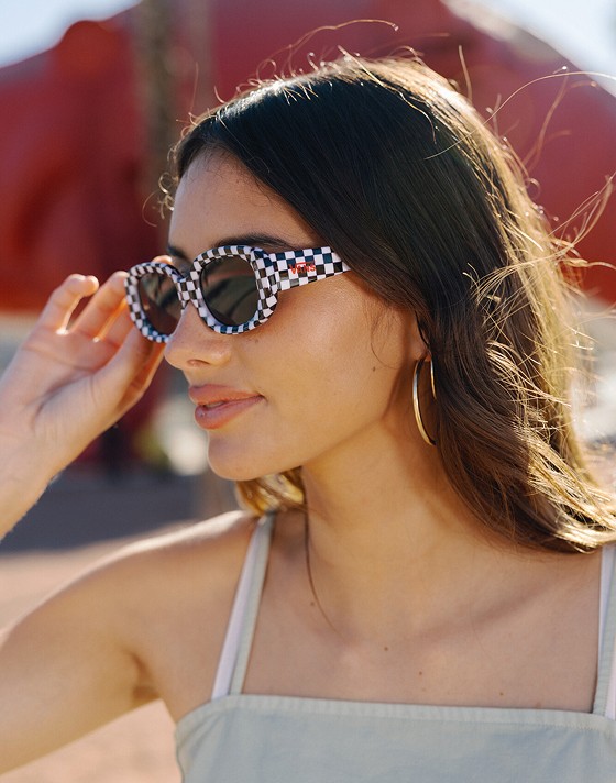 Close-up on a young woman wearing a soft sage green Crop Cami Tank Top and Checkerboard sunglasses.