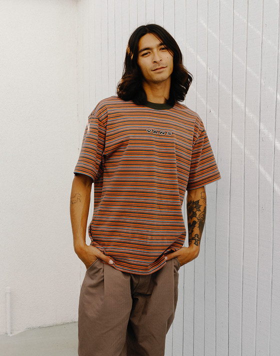 A young man looks at the camera wearing a brown and orange Cameron Stripe Knit Shirt.
