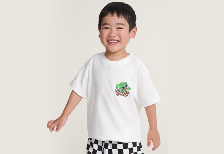 A young boy smiling at the camera wearing a Little Kids Eye Skate Glow T-Shirt and Kids Primary II Printed Elastic Boardshorts.