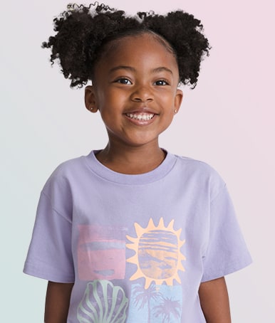 A young girl smiling at the camera wearing a purple Kids Shore Thing T-Shirt.