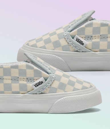 The Checkerboard Dawn Mist Blue colorway on the Toddler Classic Slip-On V Checkerboard Shoe on a lavender and light blue background.