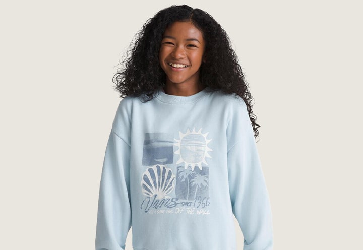 A young girl smiling at the camera wearing a light blue Kids Shore Thing Os Crew Sweatshirt.