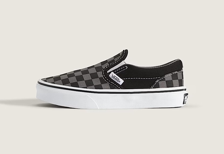 A black and gray Little Kids Knu Checkerboard Classic Slip-On in a photography studio.
