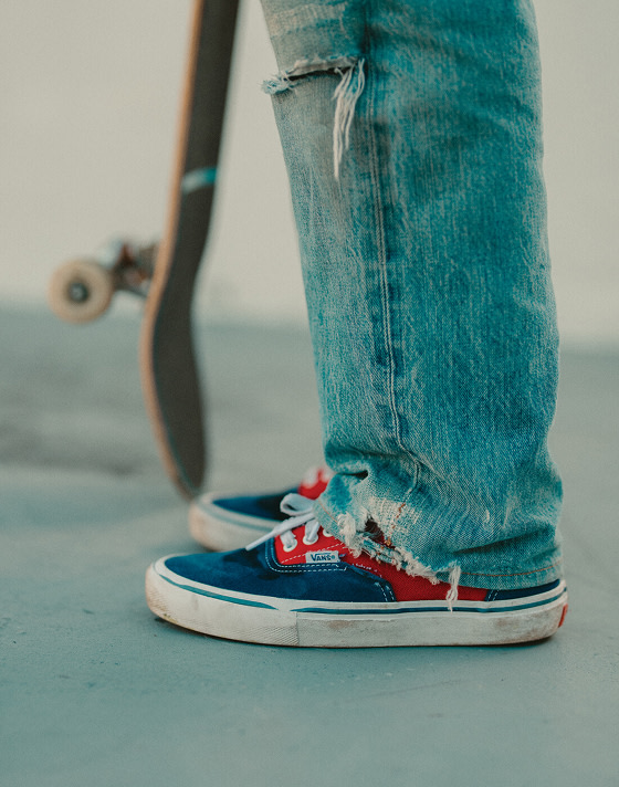 A knee-down shot of someone wearing red and blue Skate Era and holding a skateboard.