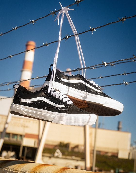 A pair of black and white Old Skool hanging from barbed wire by their laces.