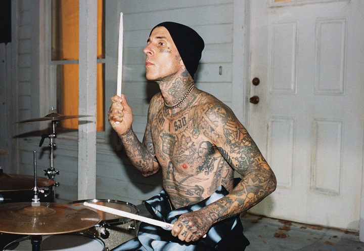 Blink-182 drummer Travis Barker drumming shirtless outside of a white house.