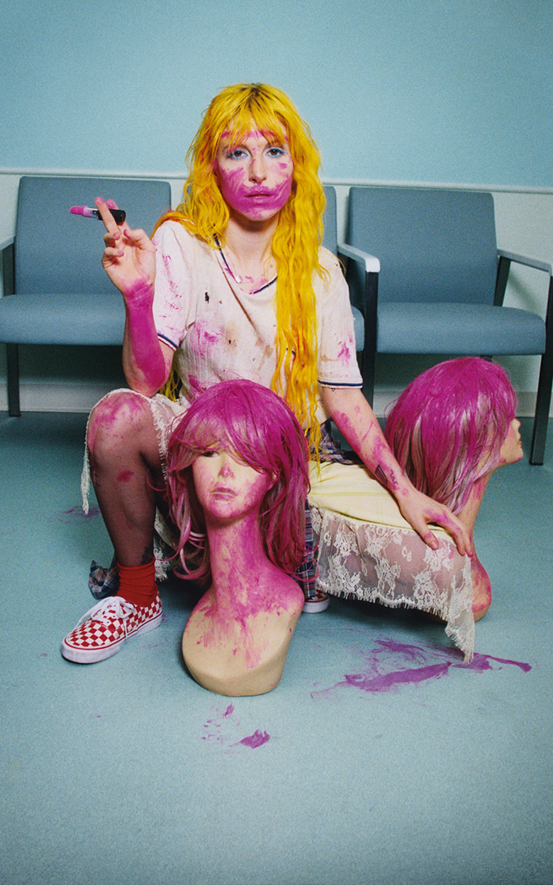 Paramore singer Hayley Williams covered in purple paint squatting next to a mannequin head and wearing red Checkerboard Authentic.