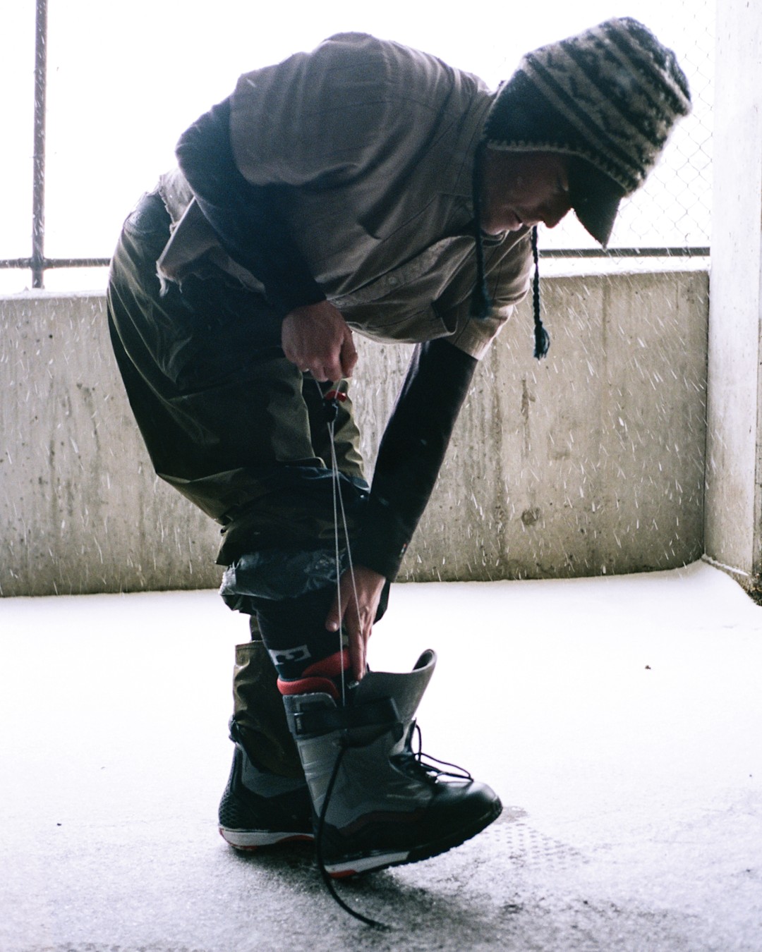 Snowboarder ties boot in a parking garage, preparing to go out and ride.