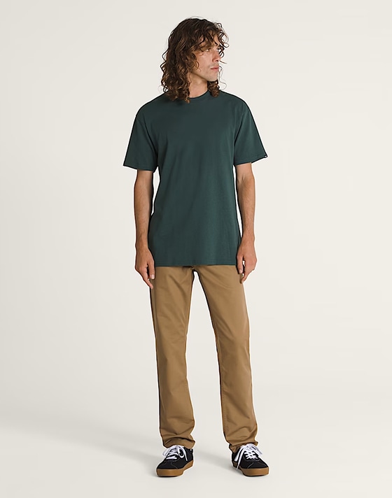 A young man poses in a photography studio wearing dirt brown Authentic Chino Slim Pants.