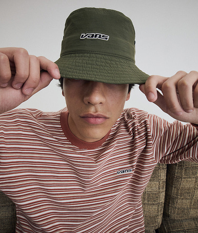 Close-up on a young man wearing a mossy olive green Dropped V Bucket Hat.