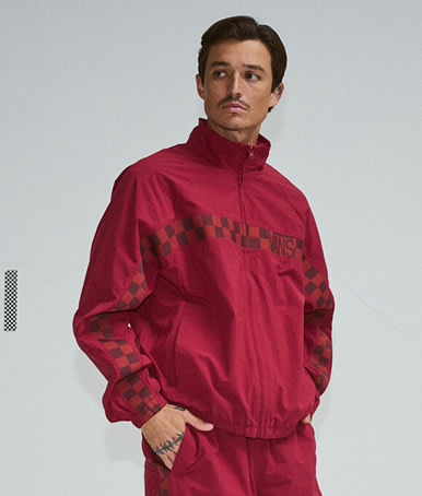 A young man poses in a photography studio wearing a bordeaux red Ronnie Track Jacket.