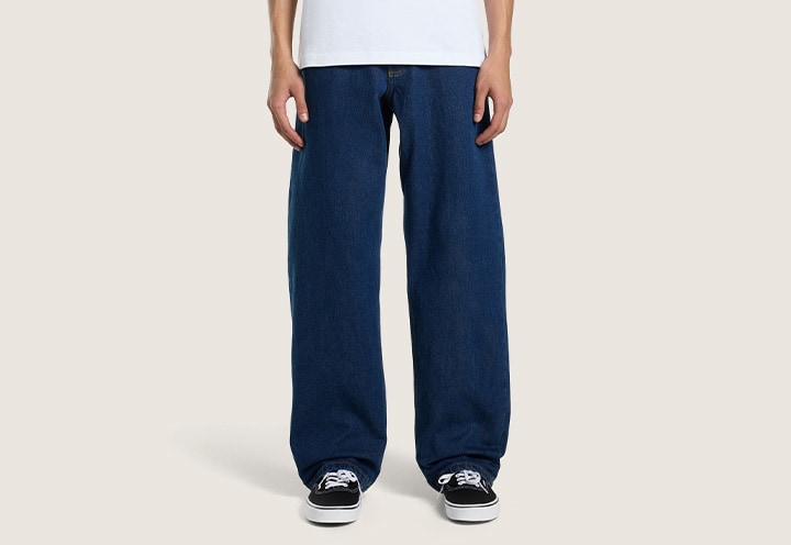 A knee-down shot of a young man wearing dark rinse blue Check-5 Loose Denim Pants.