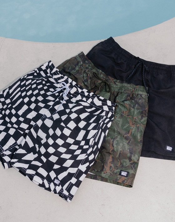 A collection of Vans board shorts laid out on a pool deck beside the water for spring break.