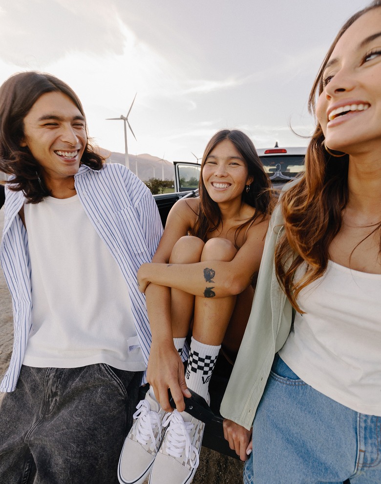 A group of friends sit in the bed of a truck on a sunny day wearing Vans clothes and shoes for Spring Break.
