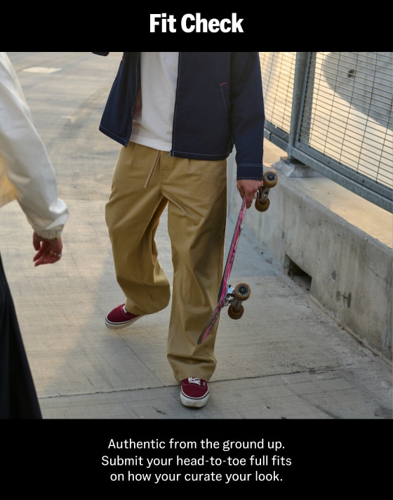 A waist-down shot of a young man wearing burgundy Authentic and incense brown Range Relaxed Elastic Pants holding a skateboard.