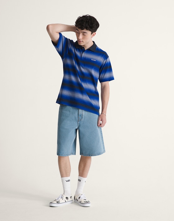 A young man posing in a photography studio wearing a royal cobalt blue Molino Shadow Stripe Polo Shirt and blue Drill Chore Loose Denim Shorts.