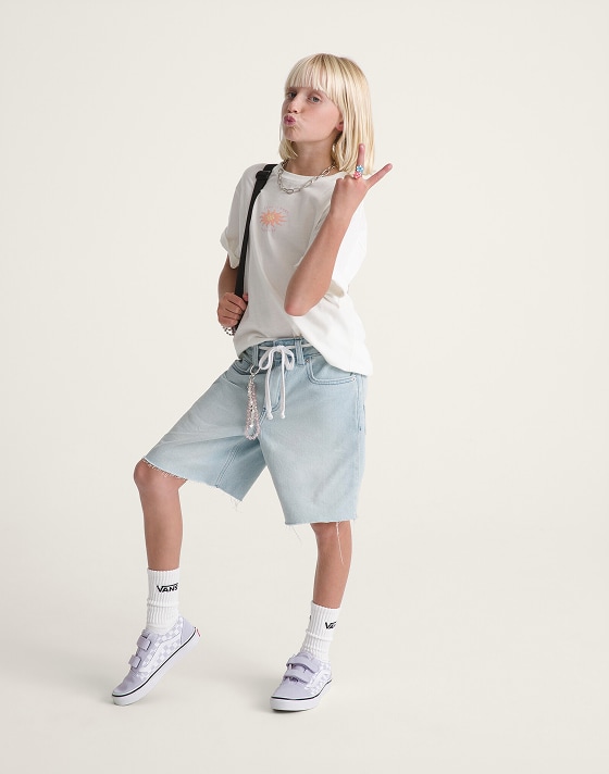 A young girl posing in a photography studio wearing a white Kids Sunny Daze T-Shirt and light stonewash blue Kids Sirelle Cut-Off Jorts.