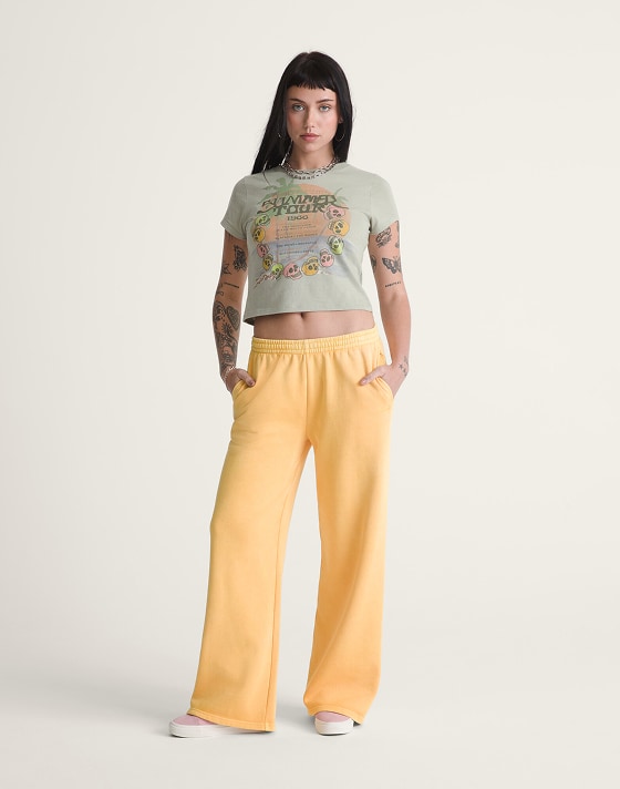 A young woman posing in a photography studio wearing spicy mustard Salton Washed Straight Fleece Pant and Summer Daze Palm T-Shirt.