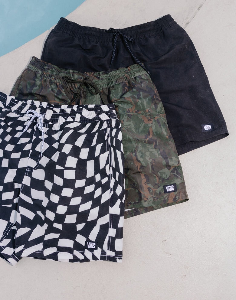 Three pairs of Kids Primary II Printed Elastic Boardshorts lay on top of each other in the Obsidian Fern Green, black and white, and black colorways.