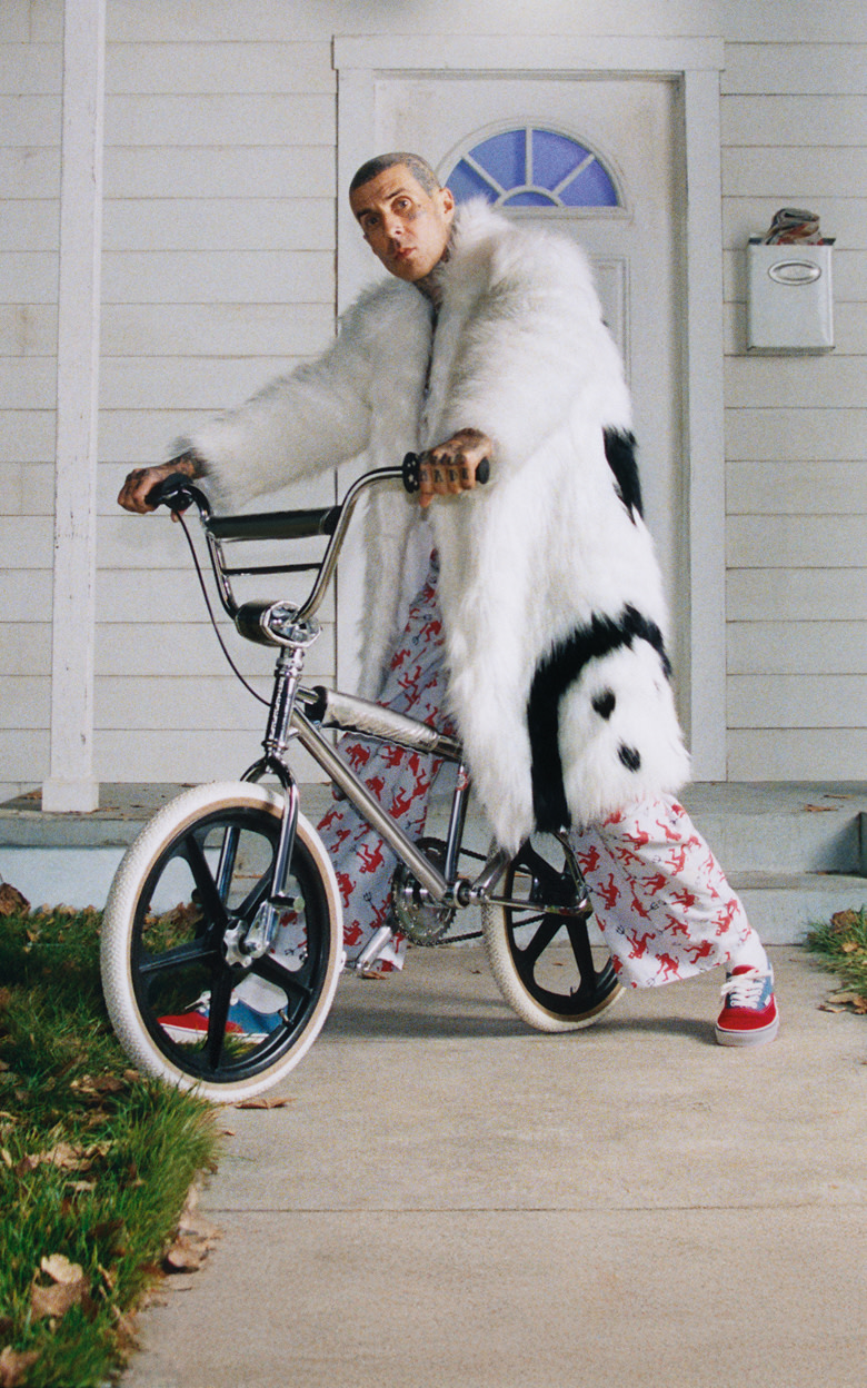 Blink-182 drummer Travis Barker sits on a bike in a fuzzy white jacket wearing red and blue Authentic from the Worn Loud Authentic Legacy drop.
