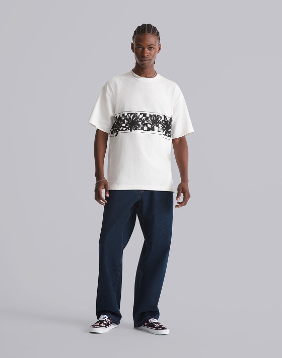 A young man posing in a photography studio wearing an egret white Palm Leaf T-Shirt and black and pink floral Authentic from the Worn Loud collection.