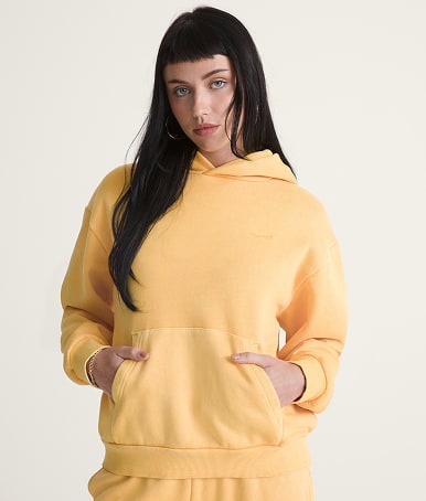 A young woman wearing a spicy mustard yellow Salton Washed Pullover Sweatshirt and Salton Washed Straight Fleece Pants in a photography studio.