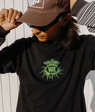 A young man fixing the fit of a vintage cocoa brown Vans Formula Snapback Hat and wearing a black Torched T-Shirt T-Shirt.