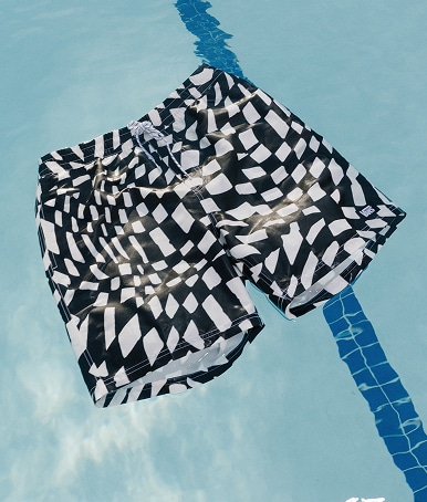 A pair of black and white Primary II Printed Elastic Boardshorts floating on top of the water in a pool.