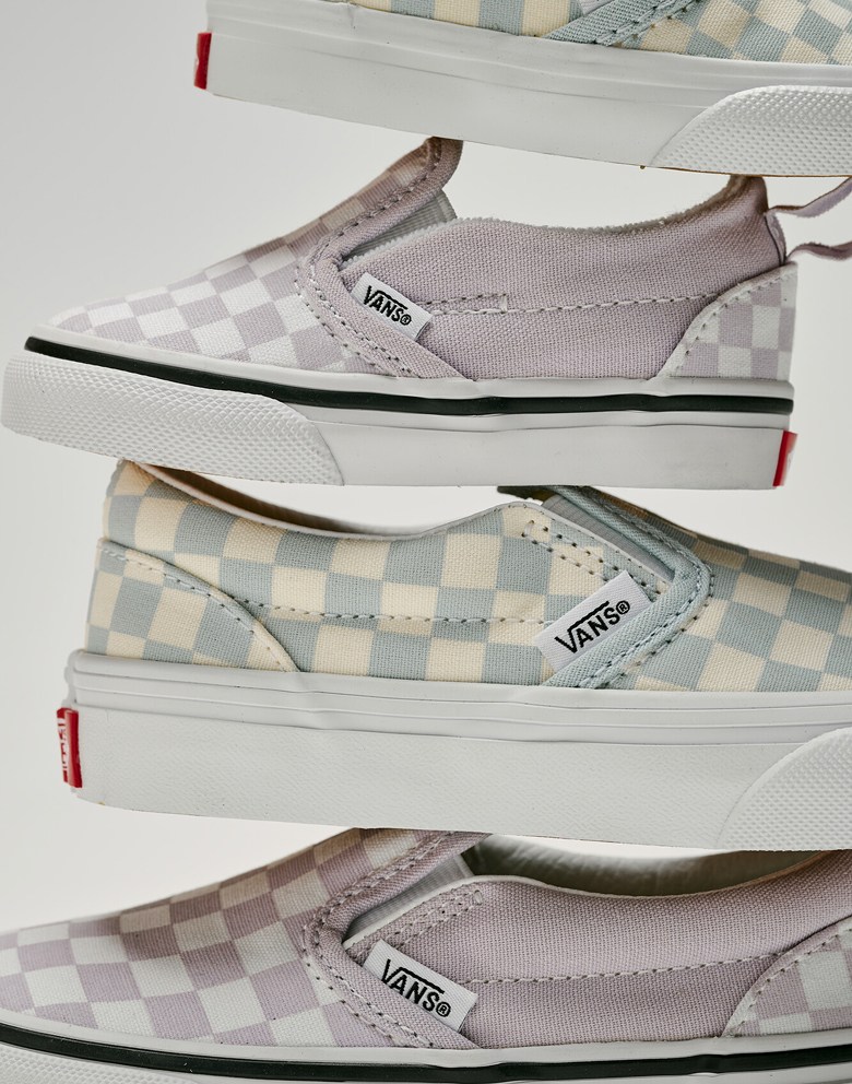The yellow and blue colorway and the lavender and white colorway of Checkerboard Classic Slip-On in different kids’ sizes in a photography studio.
