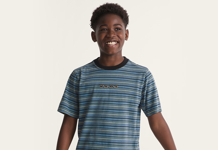 A young boy smiling and wearing a black and true blue Kids Cameron Stripe Knit Shirt in a photography studio.