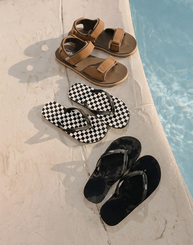 A black Makena Sandal, a Makena Checkerboard Sandal, and a chipmunk brown Tri-Lock Sandal on a pool deck next to the water.