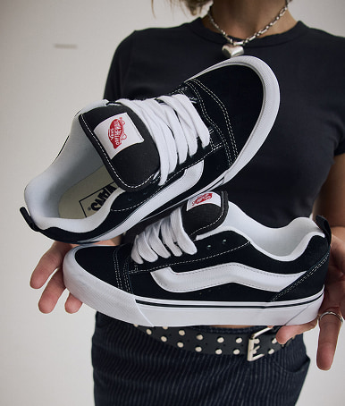 Close-up on someone holding a pair of black and white Knu Skool.