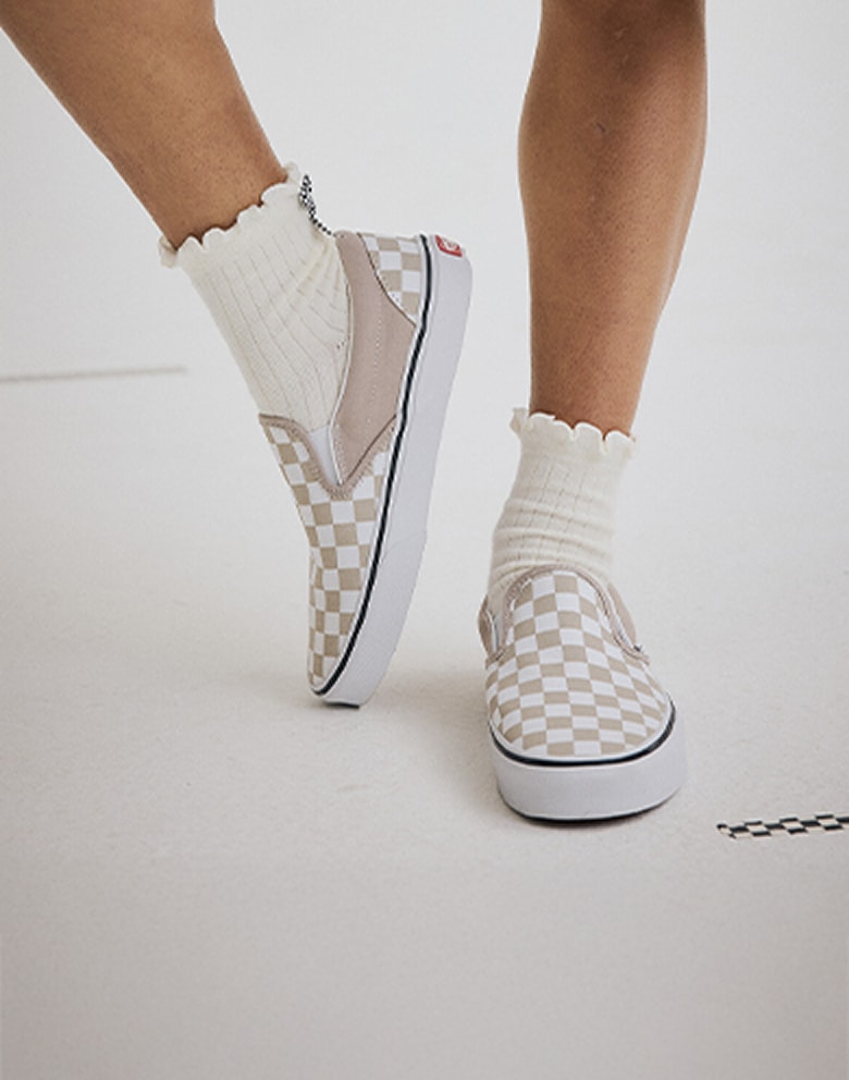 Close-up on someone wearing mushroom brown Checkerboard Classic Slip-On with white frilly socks.
