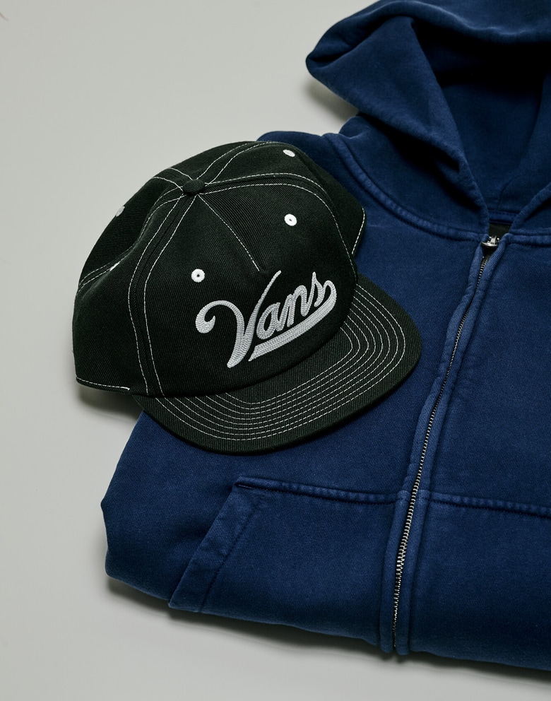 Une casquette Crestwood non structurée noire repose sur un chandail à capuchon Premium à fermeture éclair bleu dans un studio photo.