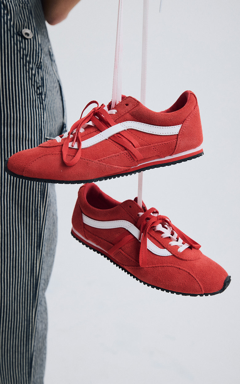 Close-up on the Super Lowpro in Racing Red being held by its shoe laces in a photography studio.