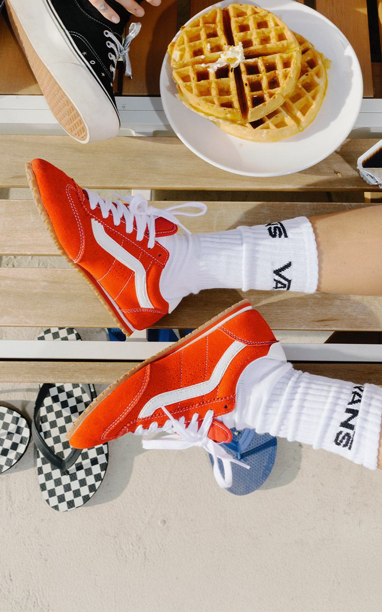 A calf-down image of someone wearing the red Super Lowpro Trainers next to a plate of waffles. 