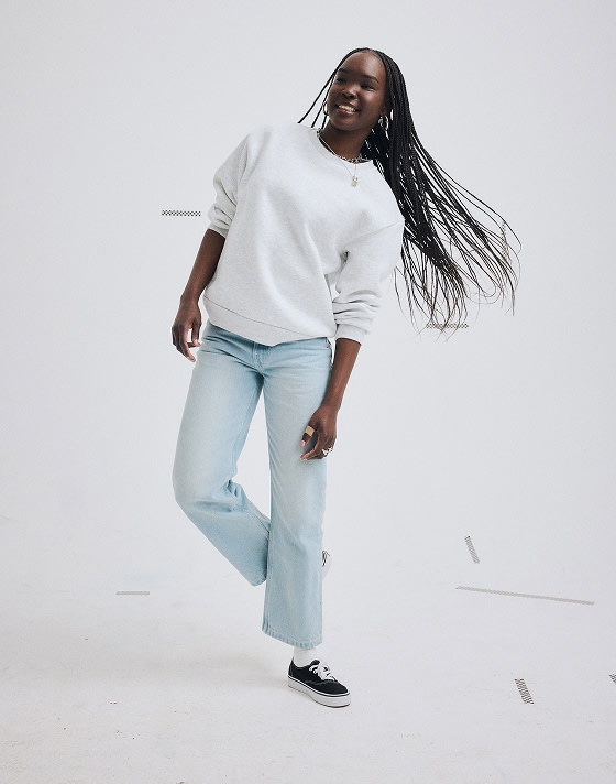 A young woman poses in a photography studio wearing a gray Premium Crewneck Sweatshirt and light stonewash blue Check-5 Mid Rise Straight Pants.