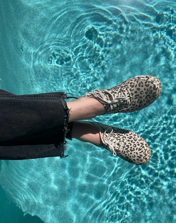 A young woman holds her feet over a pool wearing black and white leopard print Authentic.
