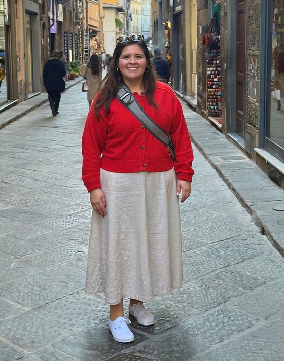 A young woman poses on a European street wearing white Authentic with a tan skirt and red cardigan.